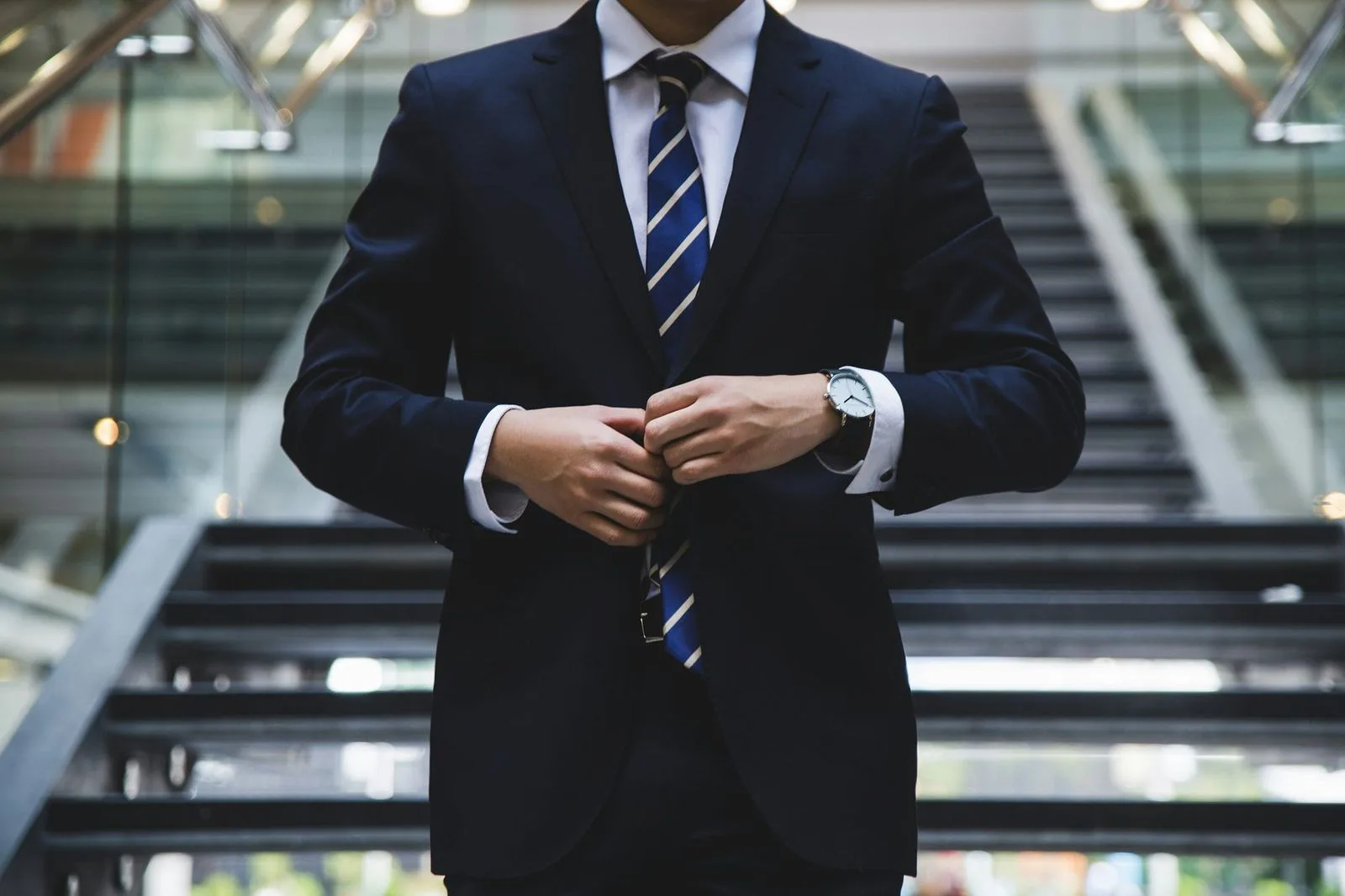 A man in a suit adjusting his cufflinks at the foot of an escalator