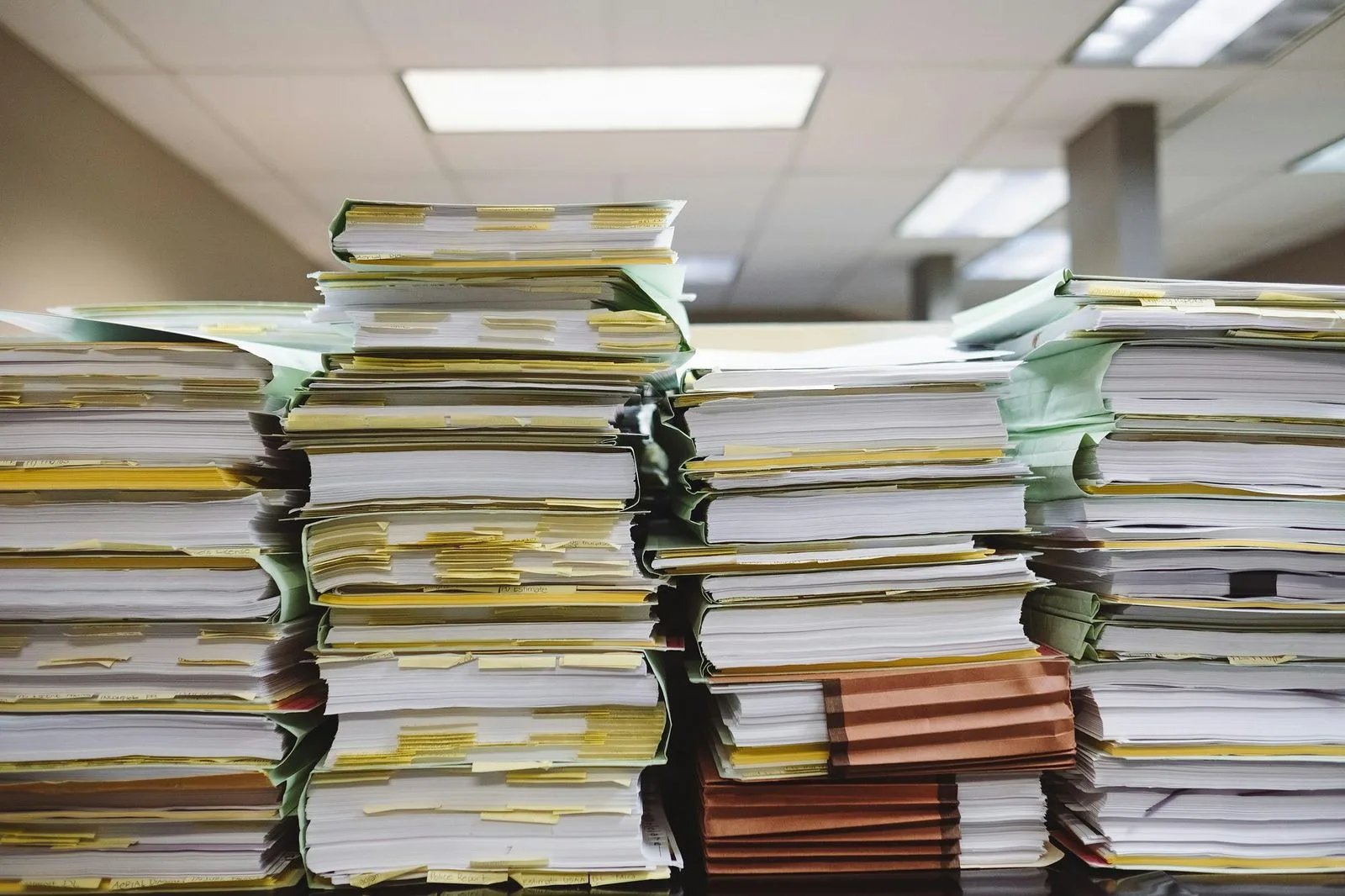 Tall stacks of paper files piled on an office desk