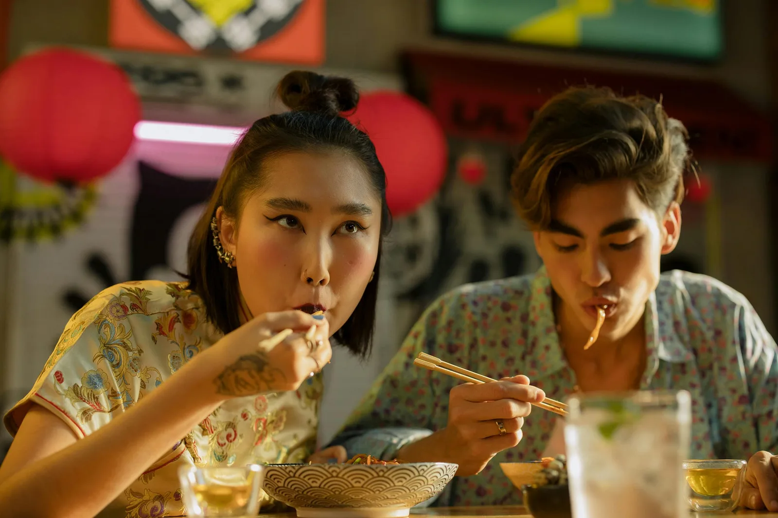 A young couple eating noodles together at a street food stall