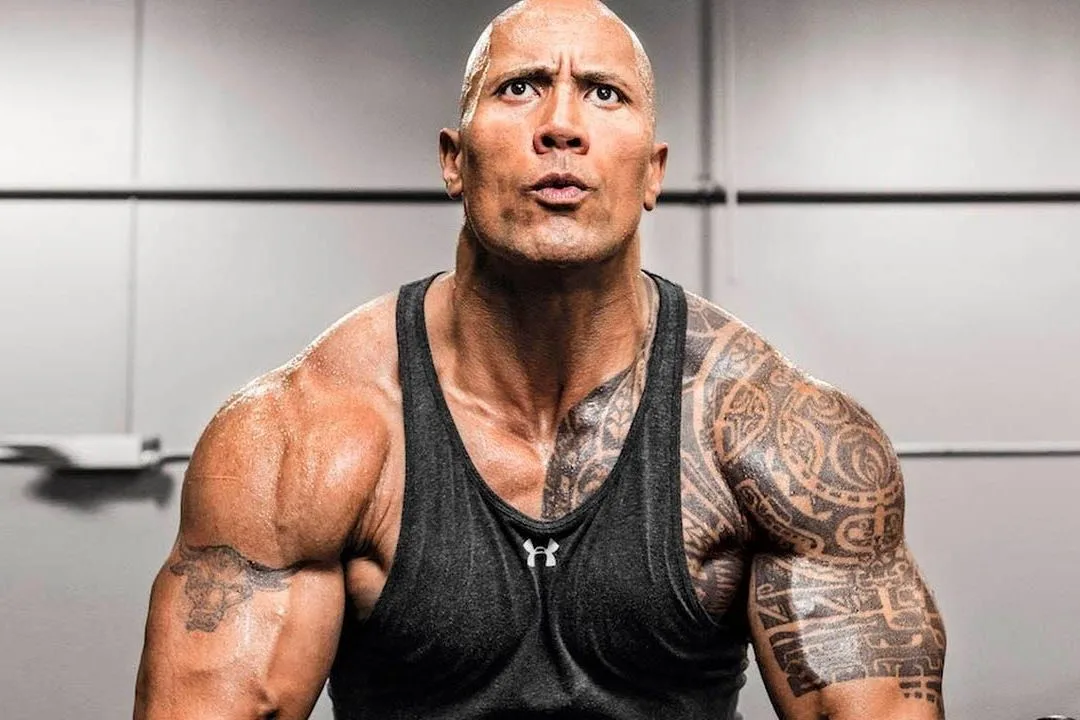 Dwayne Johnson in a gym vest, looking up between sets