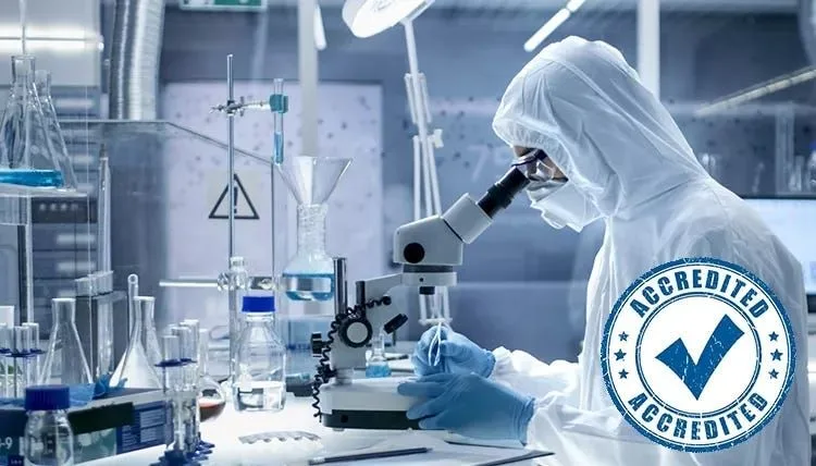 A scientist in a protective suit at a microscope in a laboratory, beside an Accredited stamp