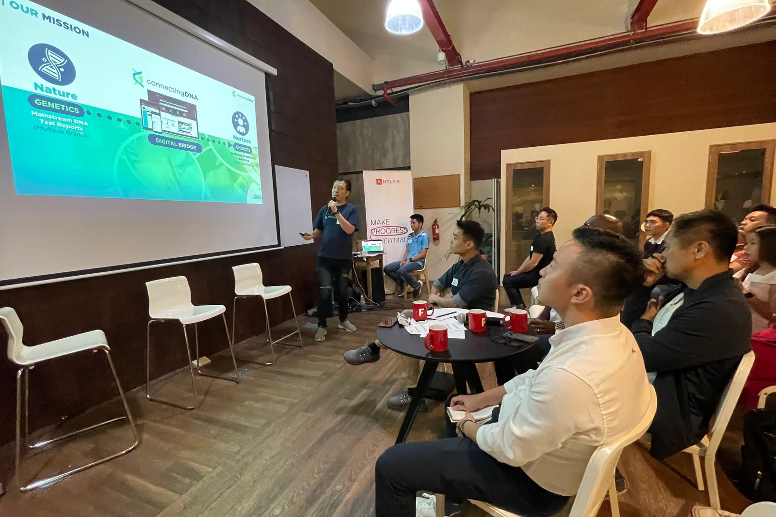 Cedric Lee presenting ConnectingDNA to a seated audience in front of a projected slide at an Antler event