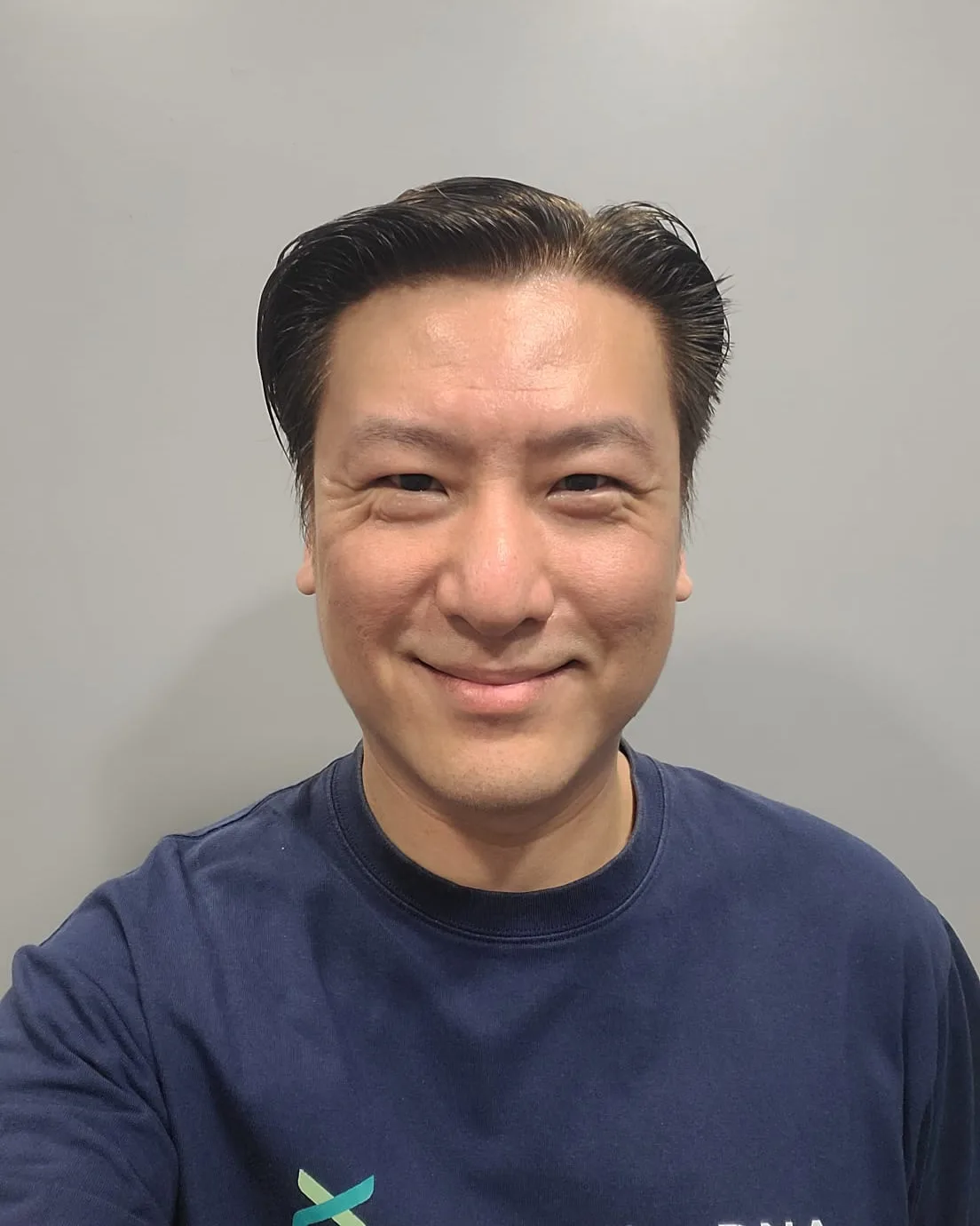 Cedric Lee smiling in a navy ConnectingDNA T-shirt against a grey wall