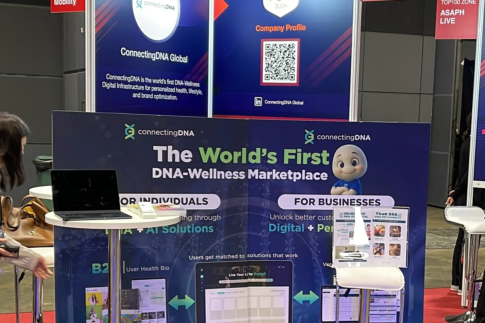 The ConnectingDNA booth at a trade show, its backdrop reading The World's First DNA-Wellness Marketplace, with a laptop on a stand at the left