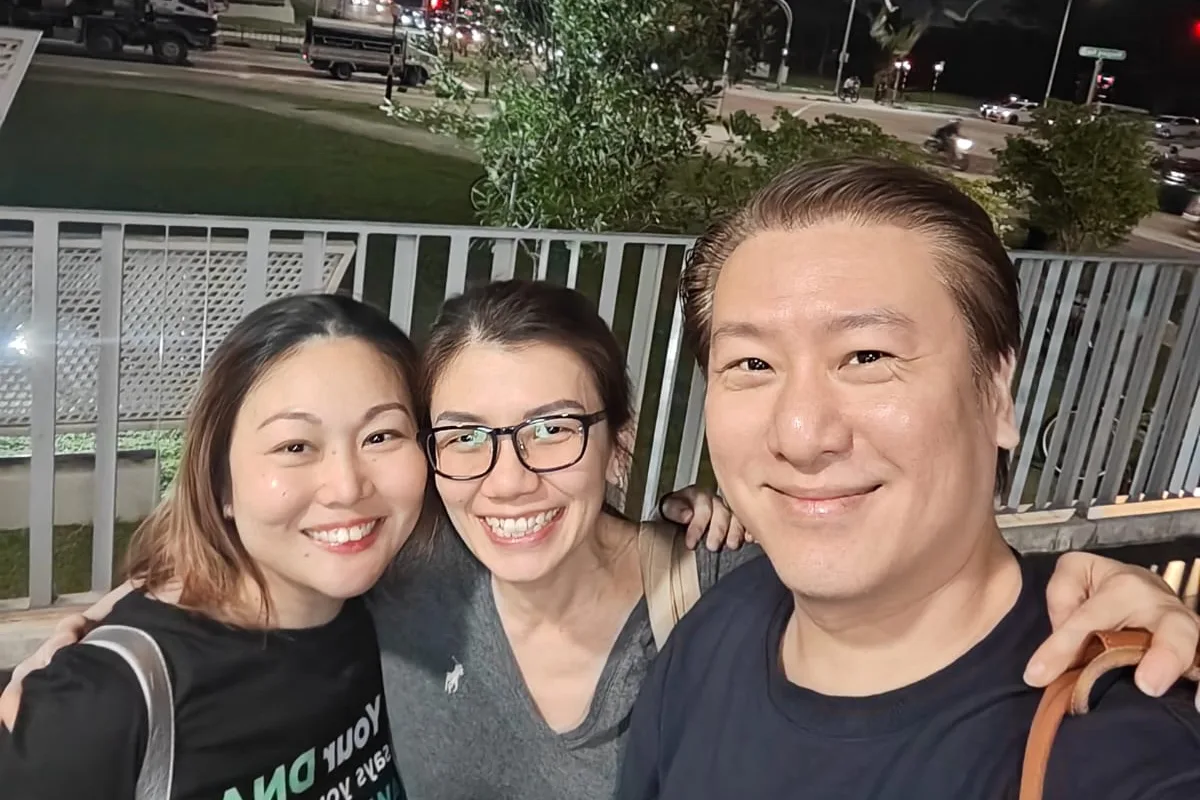 Three people smiling together at night with a road behind them