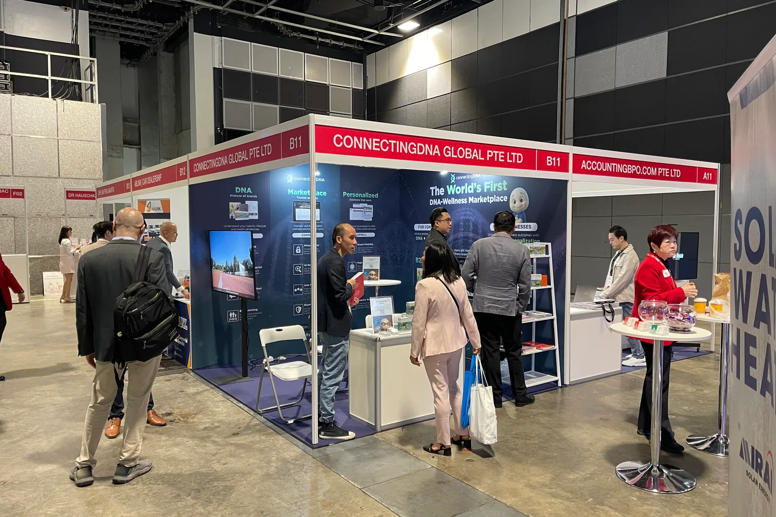 The ConnectingDNA booth at a trade show, its back wall reading The World's First DNA-Wellness Marketplace, visitors at the counter and passing in the aisle