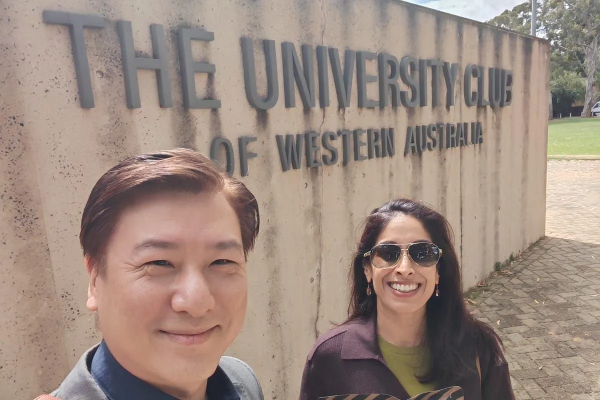 One of the ConnectingDNA team and a woman holding a snack packet beside the sign of the University Club of Western Australia