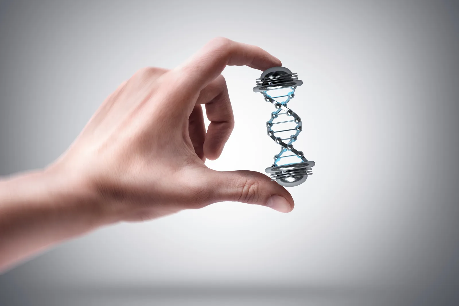 A hand holding a small model of a DNA double helix between finger and thumb against a grey ground