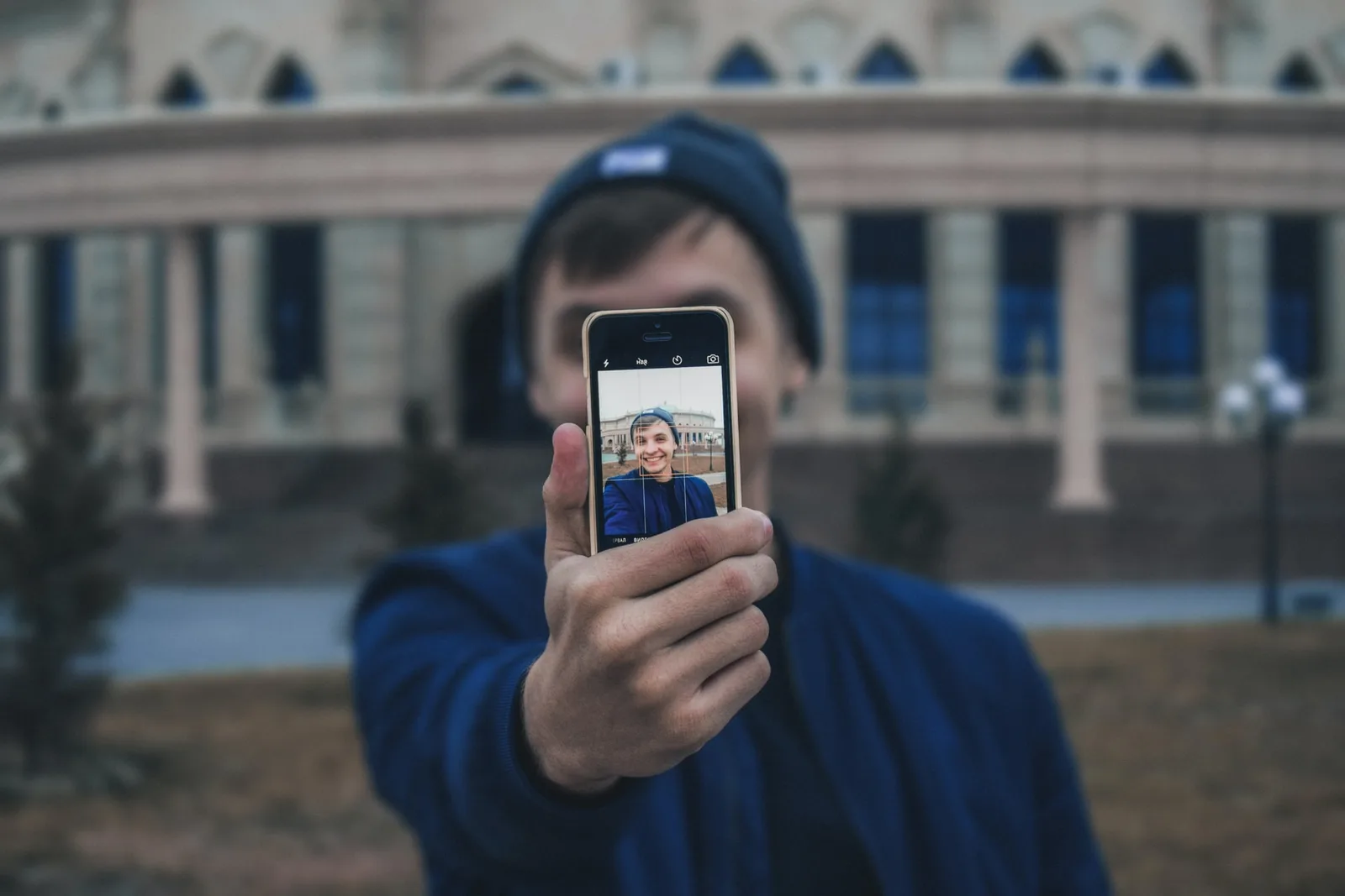 A young man in a beanie holding a phone out towards the camera, his own smiling face on its screen
