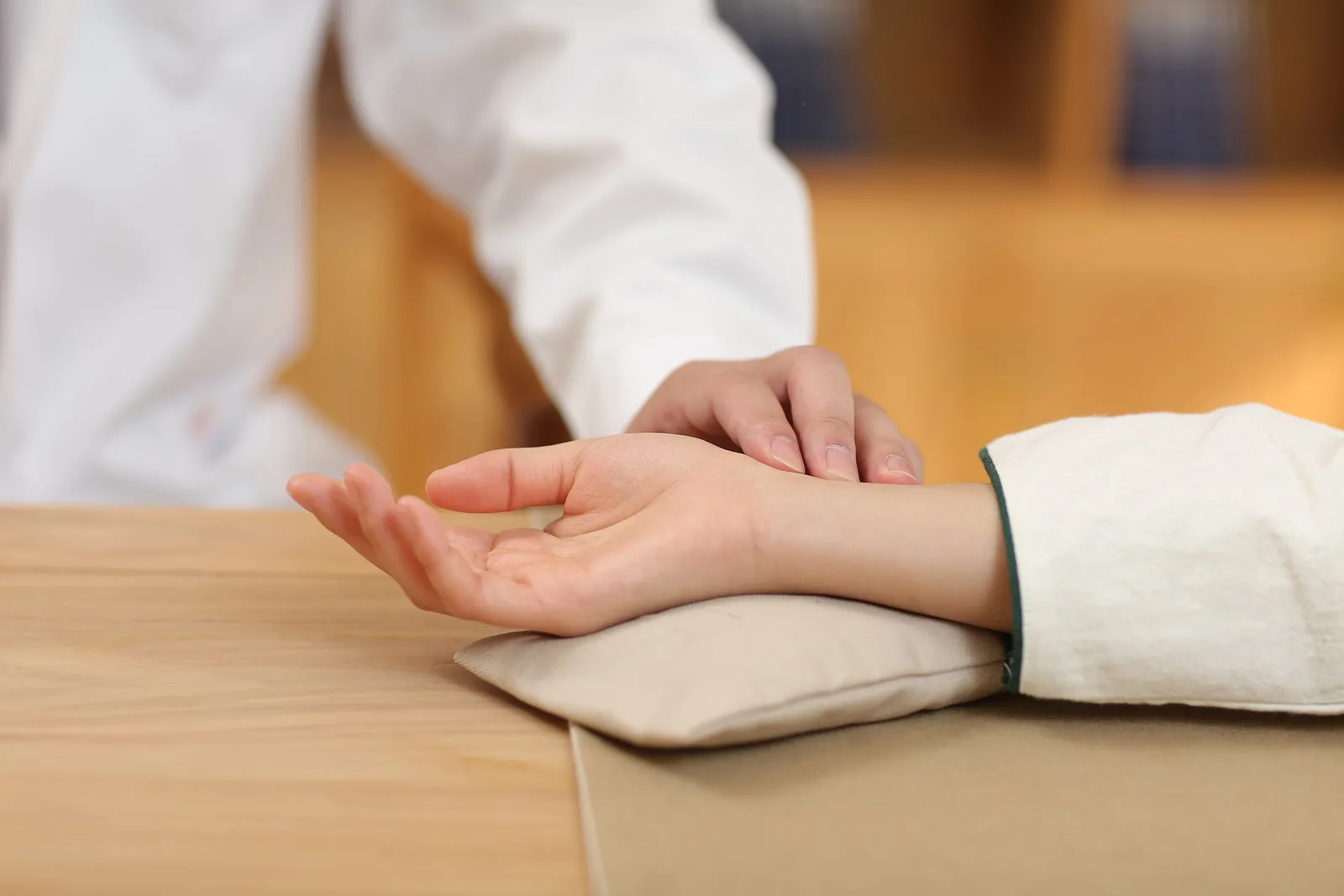 A practitioner in a white coat taking a person's pulse, the wrist resting on a small cushion