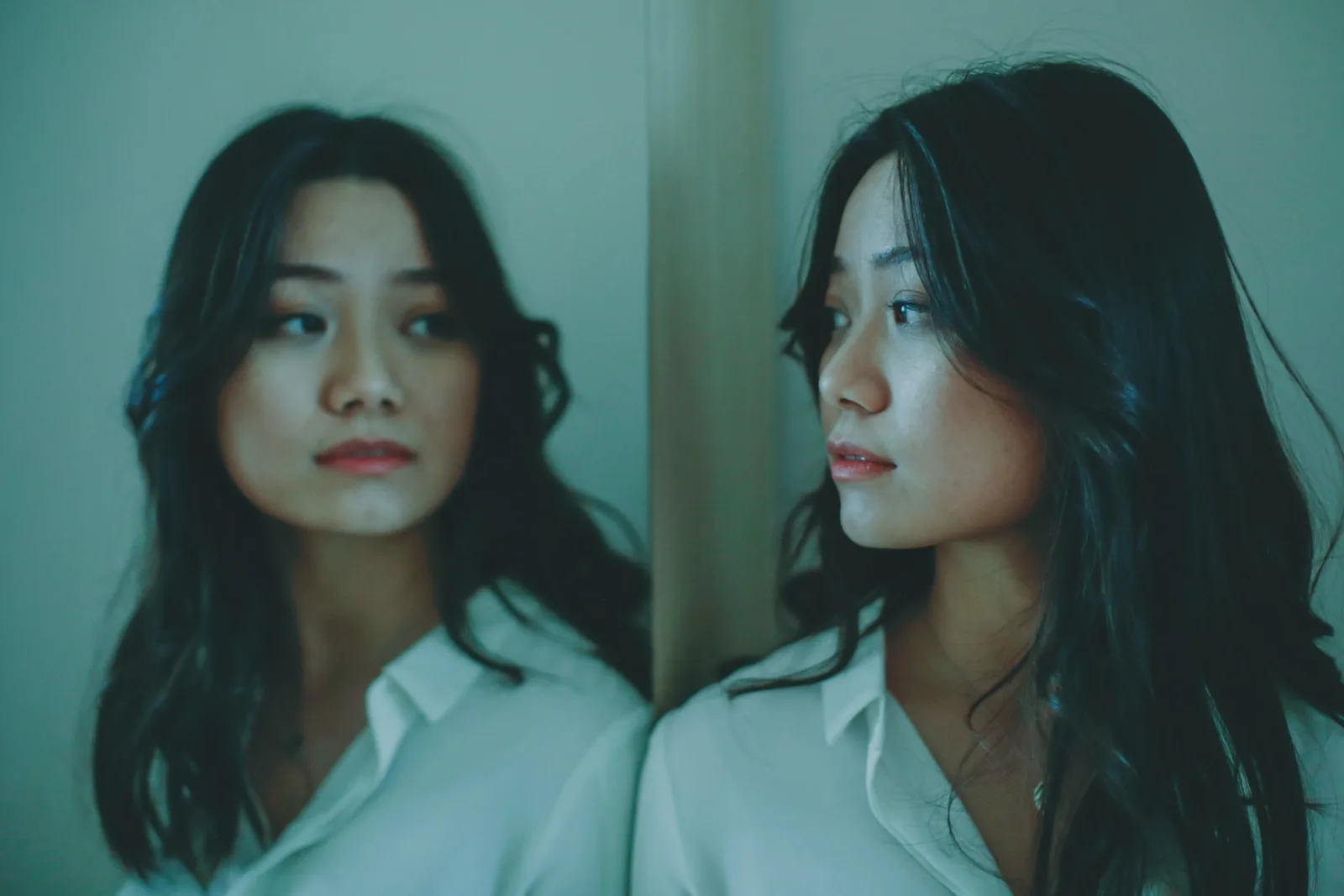 Two young women with long dark hair and white shirts side by side, one looking at the other